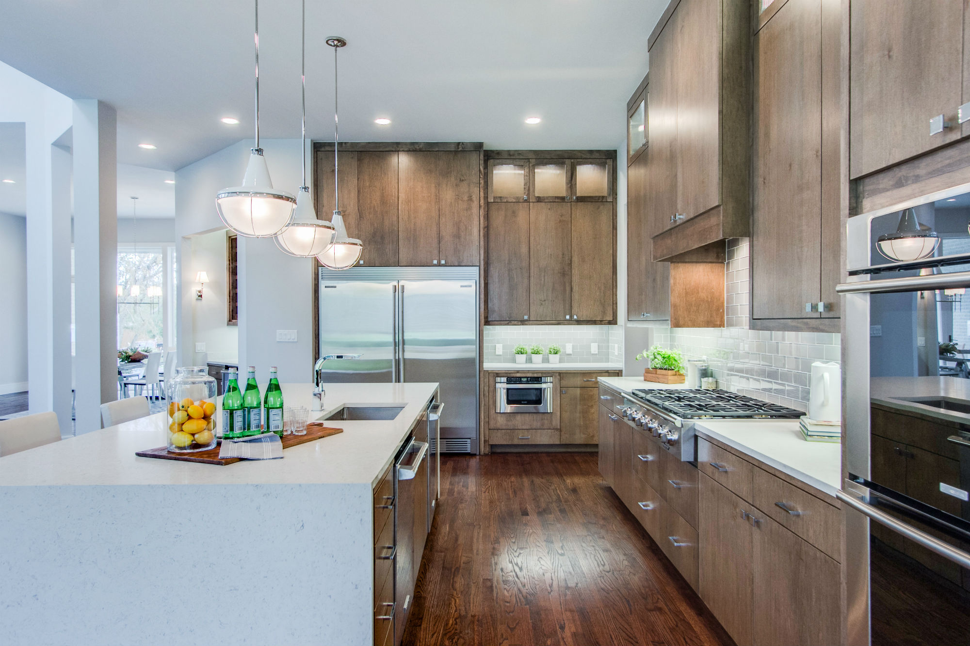 Modern kitchen featuring wooden cabinetry, a large island with a sink, and polished countertops. Green plants add a touch of freshness.