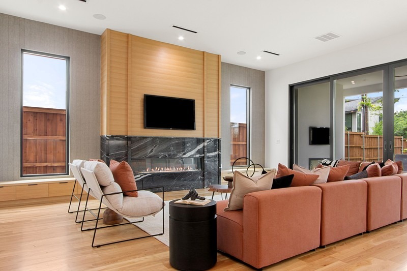 Modern living room featuring a sleek black marble fireplace, cozy orange sectional sofa, and large windows that offer natural light.
