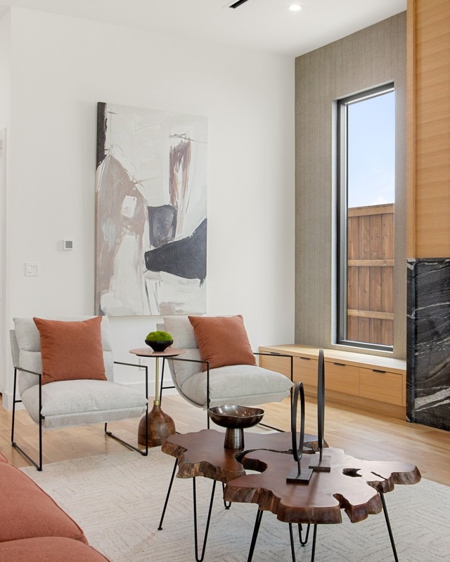 Modern living room featuring two stylish chairs with orange cushions, a unique wood and metal coffee table, and a large abstract painting.