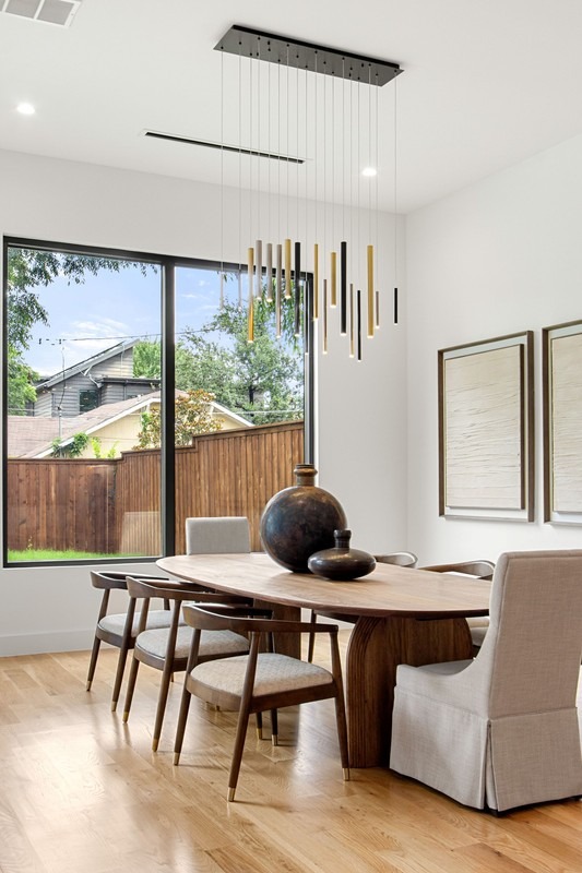 Modern dining area featuring a wooden table with decorative vases, surrounded by light-colored chairs. Large windows allow natural light.