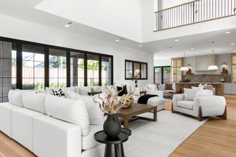 Modern living room featuring a spacious layout with white sofas, a wooden coffee table, and large windows providing natural light.