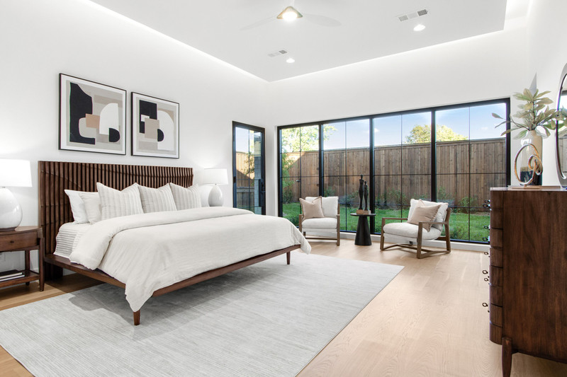 Bright modern bedroom featuring a king-sized bed, creative artwork, large windows, and a cozy seating area overlooking a garden.