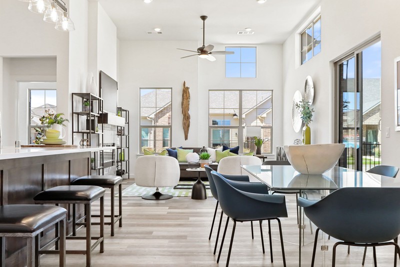 Bright, modern living space featuring a dining area with a glass table, stylish chairs, and a cozy seating area highlighted by large windows.