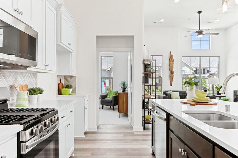 Bright, modern kitchen featuring white cabinets, stainless steel appliances, and a window view into a living area with greenery.