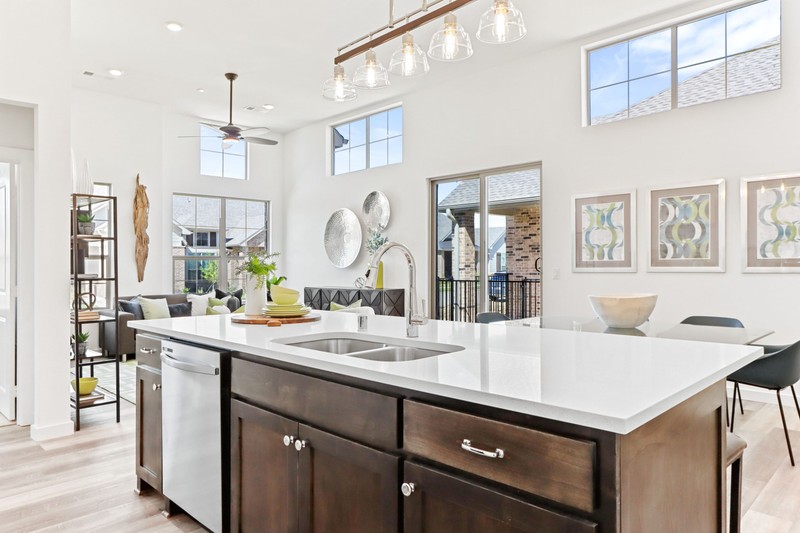 Modern kitchen with dark cabinetry and a white countertop, featuring a view of the living area and large windows, enhancing natural light.