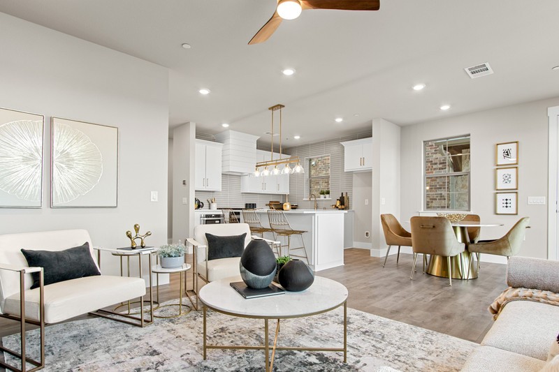 Modern living area featuring stylish white furniture, a round coffee table with decorative elements, and a bright kitchen in the background.