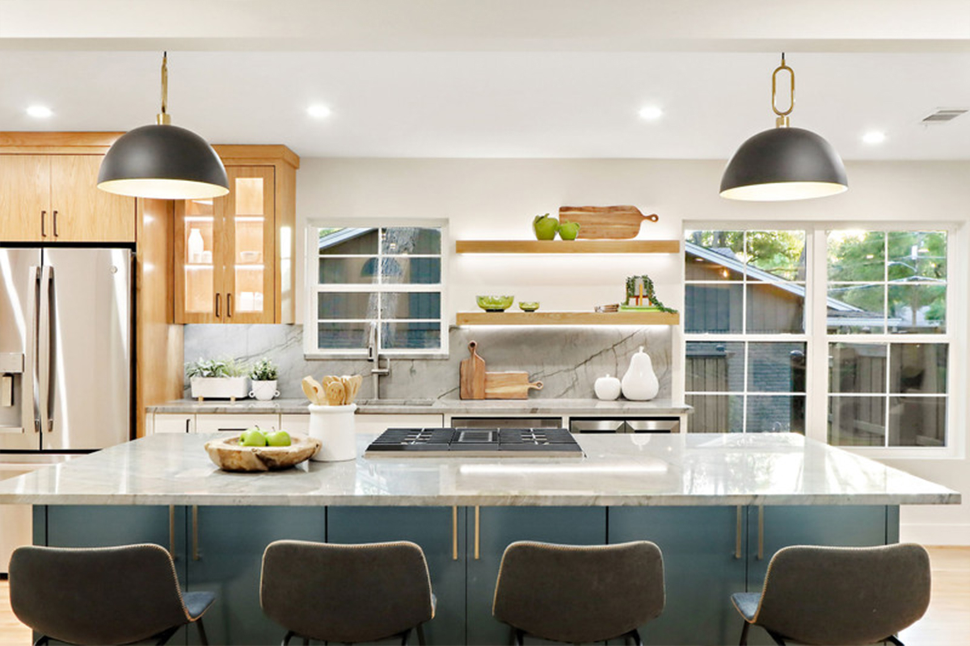 Modern kitchen featuring a central island with a marble countertop, stylish lighting, wooden cabinets, and decorative green accents.