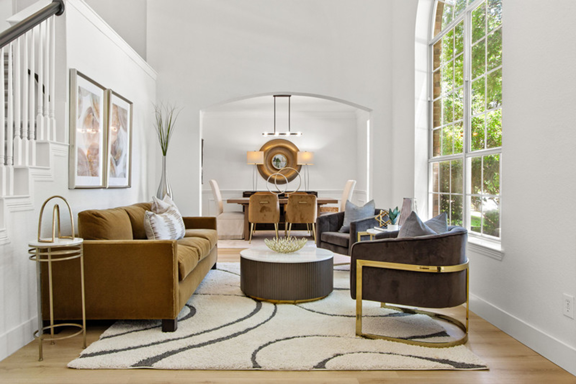 Modern living room featuring a brown sofa and black chairs, accented by a circular coffee table. Large windows provide natural light, illuminating the space.