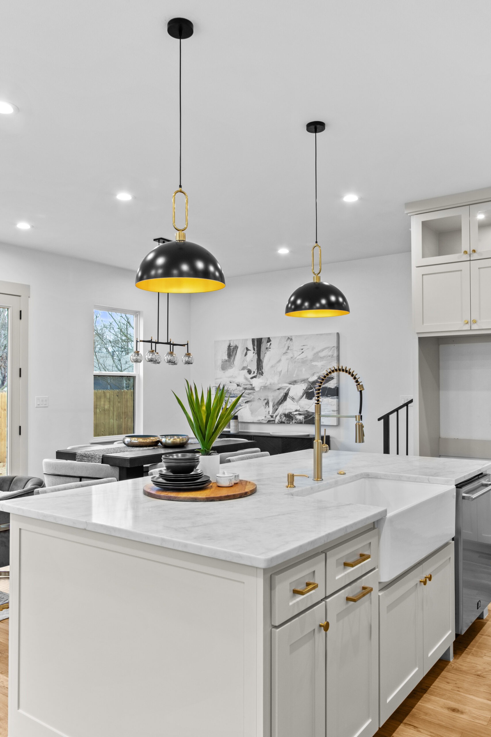 Modern kitchen featuring a marble island, brass-accented fixtures, and stylish pendant lights. A potted plant adds a touch of greenery.